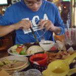 Young man in blue shirt prepares food at a restaurant table with various dishes.