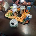 Seafood platter with shrimp and chips on a dark table, with drinks nearby.