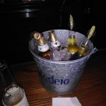 Ice bucket filled with bottles and lemon slices on a wooden table.