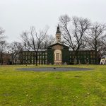 Historic brick building with a central cupola, surrounded by bare trees on a grassy lawn.