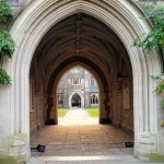 Stone archway leading through a cloister to an exterior courtyard view.