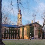 Historic university building with a clock tower, covered in ivy, under bright sky.