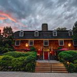 Historic wooden building under dramatic sunset sky with lush green landscaping.