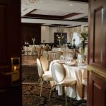 Elegant reception hall set for a formal event with tables, chairs, and chandeliers.