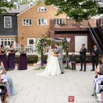 Wedding ceremony outdoors on a brick courtyard with guests watching the couple.