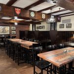Rustic pub interior with dark wood paneling, high ceilings, and long wooden tables.