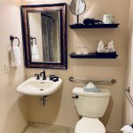 Modern bathroom with white sink, mirror, toilet, and shelf decor.