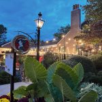 Evening view of a brick building with outdoor lighting, featuring lush foreground foliage.