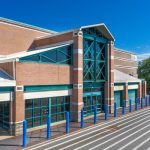 Modern brick building with glass facade and blue bollards on a sunny day.