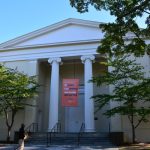 Neoclassical courthouse with columns under a clear blue sky, featuring a banner.