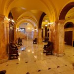 Grand, warmly lit hallway with arched ceilings and marble columns.