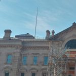 Historic building facade with a golden dome and construction scaffolding under a blue sky.