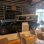 Vintage dark blue antique car displayed indoors with wooden walls and high ceilings.