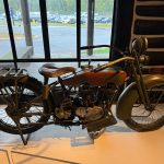 Vintage Harley-Davidson motorcycle displayed indoors with a view of a parking lot through large windows.