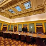 Ornate conference room with coffered ceiling, large table, and chairs for a meeting.
