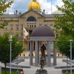 Dome-topped building with a statue in the foreground of a public square.