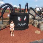 Child stands in front of a large, black, monster-themed playground structure.