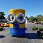 Giant yellow and blue Minion sculpture on a paved outdoor area under a clear blue sky.