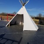 White teepee tent structure on a dark paved area under a clear blue sky.