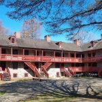 Historic brick building with wooden balconies under a blue sky and tree canopy.