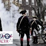 Historical reenactors in period dress stand on a wet, cobblestone street under falling snow.