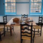Dining room with wooden table set for a meal, featuring blue-framed windows.
