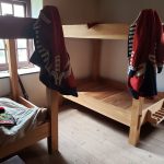 Wooden bunk beds with bedding and folded blankets, featuring a window in the background.
