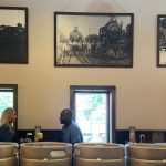 Three historical train photos hang above rows of metal beer kegs in a bar setting.