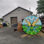 Colorful mural of corn and wheat on a gravel lot near a metal barn.