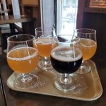 Assortment of beer glasses on a tray in a dimly lit bar setting.