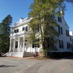 White historic mansion with columns and trees on a sunny day.
