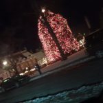 Christmas tree lit with red lights on a snowy city street at night.