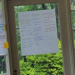 Handwritten community board visible through a window overlooking green trees.