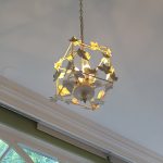 Ornate brass chandelier with floral accents hanging in a room with large windows.