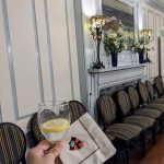 Wine glass held near a dining table with chairs and fireplace decor.