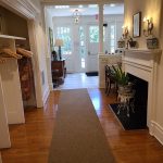 Bright entryway with hardwood floors, neutral rug, and view into a sunlit living area.