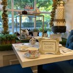 Elegant tea party display with tiered cake, floral arrangements, and a reserved sign on a white table.