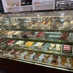 Display case filled with various cakes, pastries, and desserts in a bakery setting.