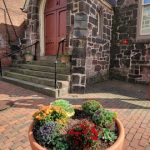 Terracotta planter with colorful flowers in front of a historic stone church.