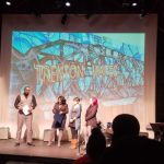 Performers on stage under a large screen displaying "Trenton Wales" graphic.