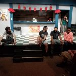 Group of young adults seated on a stage in front of a storefront window display.