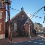 Historic stone church and brick building on a sunny city street.