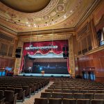 Ornate theater interior with tiered seating facing a large stage and proscenium arch.