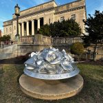 Silver rose sculpture on a pedestal in front of a classical government building.