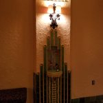Ornate wall sconce illuminates a decorative niche with tiles in an interior hallway.