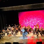 Live band performing on stage with a vibrant, bright pink sparkling backdrop.