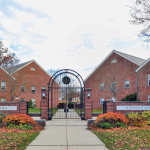 Brick school building entrance with arched gate and autumn foliage.
