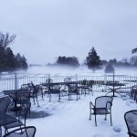 Snow-covered outdoor patio with tables and chairs under a foggy, winter sky.