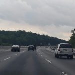 View from a moving car on a multi-lane highway under an overcast sky with trees lining the sides.