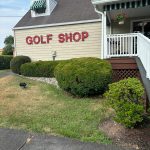 Golf shop building with red lettering, green landscaping, and white porch.